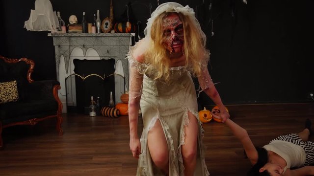 Murder victim dragged on floor by hand by creepy zombie bride dead wife in professional Halloween makeup bridal gown