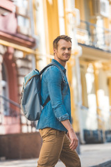 attractive young traveller with backpack walking by street and looking at camera