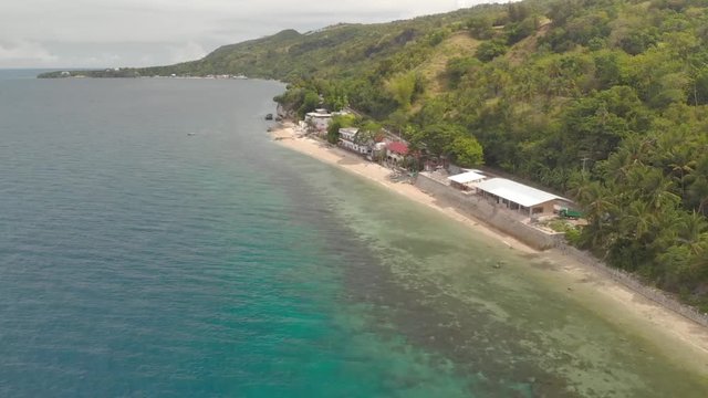 Aerial Drone shot flying over clear blue water, towards a bus on a road, on a coast full of resorts, on Cebu island, in Philippines, Asia