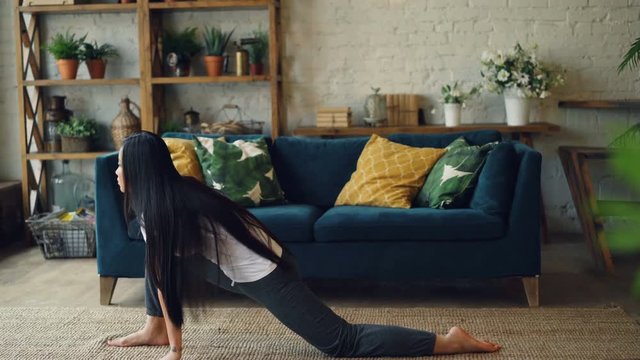 Slender Asian sportswoman is practising leg-split at home sitting on floor then bending forward during personal practice alone. Gymnastics and youth concept.
