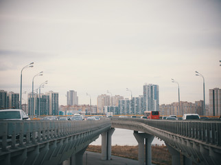 Obraz premium Cars go on bridge-roads on the background of the daytime overcast city