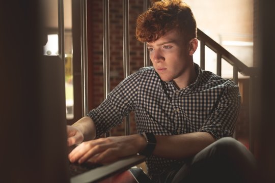 Redhead boy using laptop while sitting on stairs