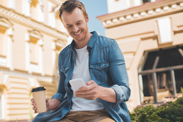 happy young man with coffee to go using smartphone on street