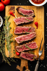 Slices of beef steak on meat fork on wooden cutting board.