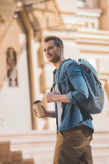 happy young man with coffee to go and backpack walking by city