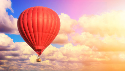 Obraz premium Red balloon against a blue cloudy sky. Sun rays and glare. Dreamy clouds. Aerostat. People in the basket. Fun. Summer entertainment. Romantic adventures.