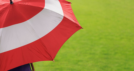 Austria flag umbrella. Close up of printed umbrella over green grass lawn / field. Rainy weather forecast concept.