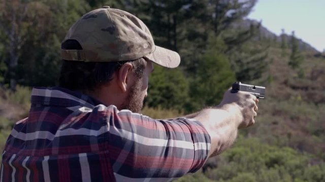 Over the shoulder shot of a man shooting a handgun outdoors