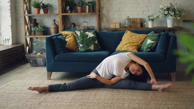 Slender Asian lady is doing sports at home stretching body, arms and legs in seated position on floor enjoying activity and healthy lifestyle. Sport and millennials concept.