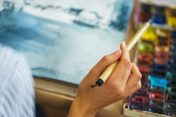 Artist makes the brush strokes on a canvas while painting a watercolor.