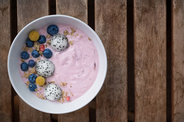 White bowl full of yogurt with blueberries, oatmeal, dragon fruit and cute yellow flower