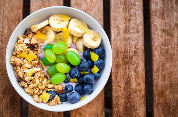 A bowl filled with oatmeal flakes of grapes, blueberries, bananas and yogurt laid on a wooden table