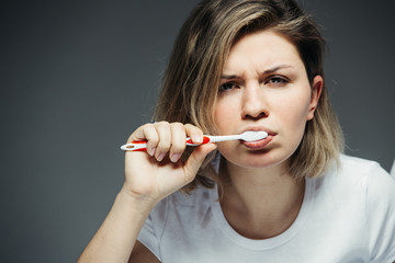 Young woman brushing her teeth. Her face is sullen and sleepy.
