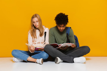 Photo of bored or upset students 16-18 using reading books while sitting on floor with legs...