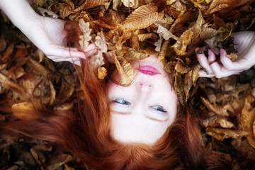Portrait eines jungen reizenden Mädchens mit freien Schultern, bedeckt mit roten und orangenen herbstlichen Blättern. Schönes sexy Mädchen auf Herbstlaub liegend,.