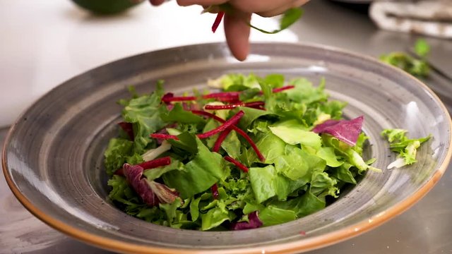 Cook placing pieces of grenery in a plate with salad. Close up spin in 4K footage