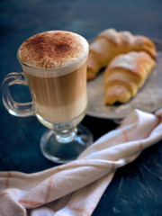 A cup of fresh coffee with croissants on a dark blue background, selective focus