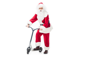 santa claus in costume standing with kick scooter and looking away isolated on white background