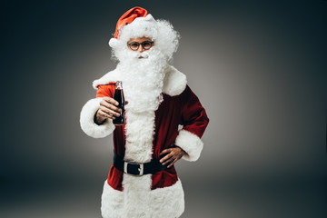 smiling santa claus in costume standing with cream soda bottle isolated on grey background