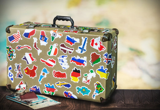 old suitcase with stikkers on the floor against the backdrop of a world map. Toned image
