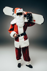 santa claus in ski mask holding snowboard over shoulder on grey background