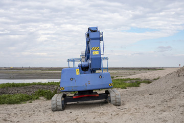 Fototapeta na wymiar A blue tractor at the marker wadden, an artificial archipelago in the Markermeer, a lake in the Netherlands, wetlands made, with blue cloudy sky.