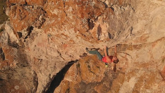 Aerial shot of young brave woman climber climbs the rock breaks, falls down and hangs on a safety rope. Slow motion.