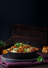Fried chanterelle mushrooms with potatoes in frying pan on dark background.