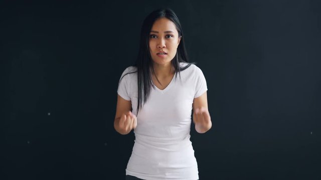 Portrait of furious Asian girl yelling and gesturing shaking fist expressing negative emotions against black background. Young people, problem and anger concept.