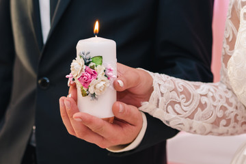 White candle with a decoration of flowers in the hands of the newlyweds. The concept of the family hearth