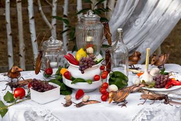 Dekoratives Garten Stillleben mit buntem Obst und Gemüse und kupfernen Vögeln sowie Käfern auf nostalgischen Gefäßen