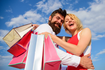 Shopping brings positive emotions. Man beard and blonde girl enjoy buy clothing. Family bought excellent clothes. Happy couple satisfied purchases. Couple with shopping bags hugs blue sky background