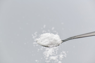 Spoon filled with sea salt on gray background.