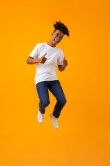 Happy young african man jumping isolated over yellow background showing thumbs up.