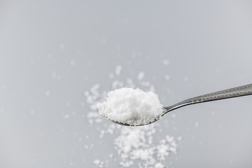 Spoon filled with sea salt on gray background.