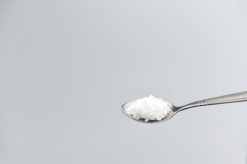 Spoon filled with sea salt on gray background.