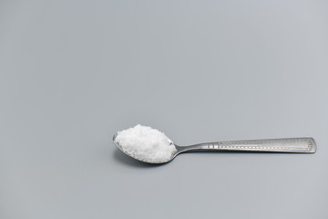 Spoon filled with sea salt on gray background.