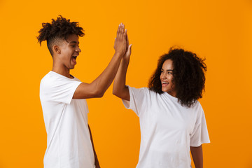 Excited emotional young cute african couple posing isolated over yellow background give a high five...