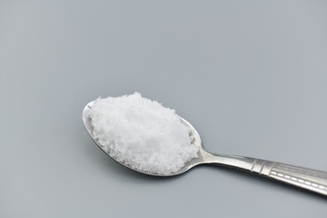 Spoon filled with sea salt on gray background.
