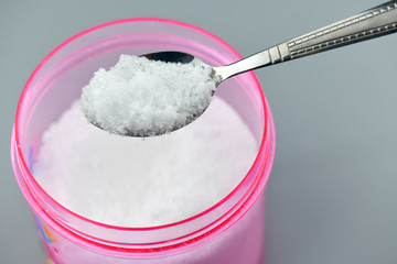 Pink bowl and spoon with salt on gray background.