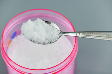 Pink bowl and spoon with salt on gray background.