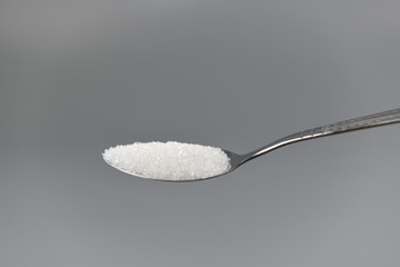 A spoonful of granulated sugar on gray background