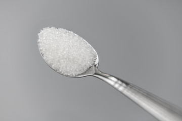 A spoonful of granulated sugar on gray background