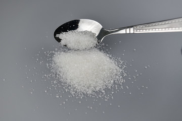 A spoonful of granulated sugar on gray background