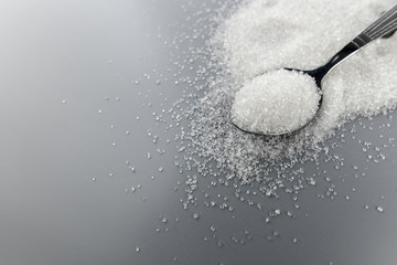 A spoonful of granulated sugar on gray background