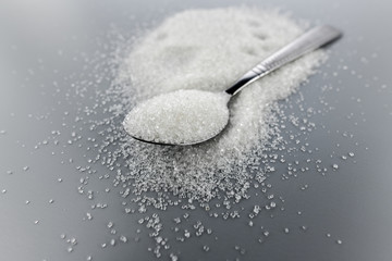 A spoonful of granulated sugar on gray background