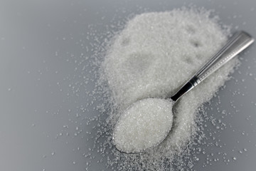 A spoonful of granulated sugar on gray background