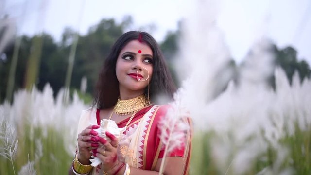 A romantic and thoughtful Indian married woman looks away holding a conch shell or shankha in a field  of white flowered grass at sunrise or sunset, beautiful and happy