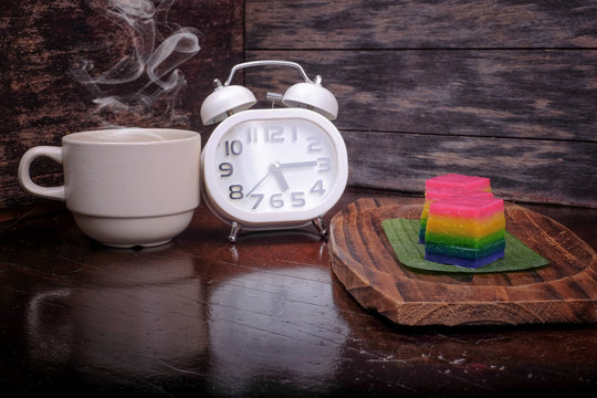Traditional Malaysian food. Kuih Lapis , alarm clock and  a cup of coffee on wooden background. Coffee time concept