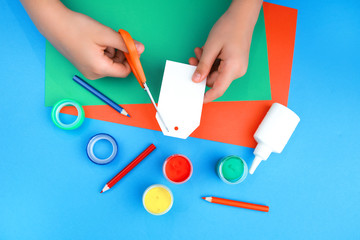 color paper, paint and hands of a child cutting paper with scissors on blue background with copy space